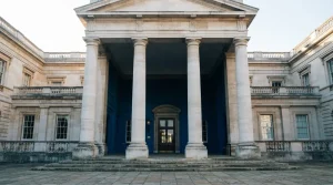 Helle Steinfassade mit vier hohen Säulen und geometrisch gegliedertem Eingangsbereich